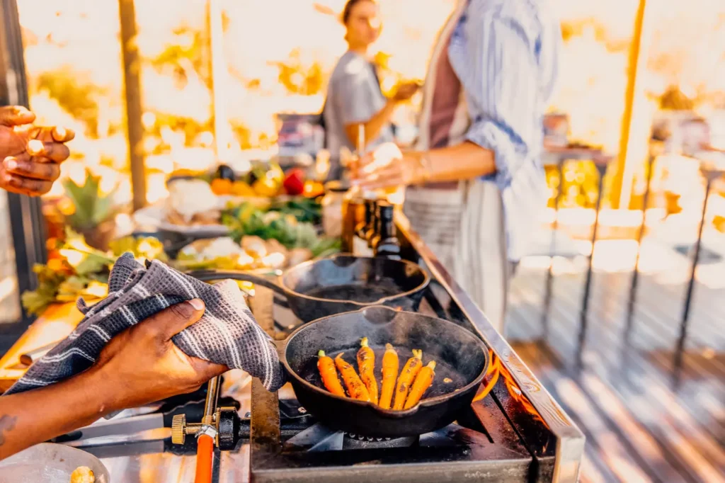 Baby carrots cooking in a cast iron pan during an outdoor cooking class at Bliss and Stars retreat