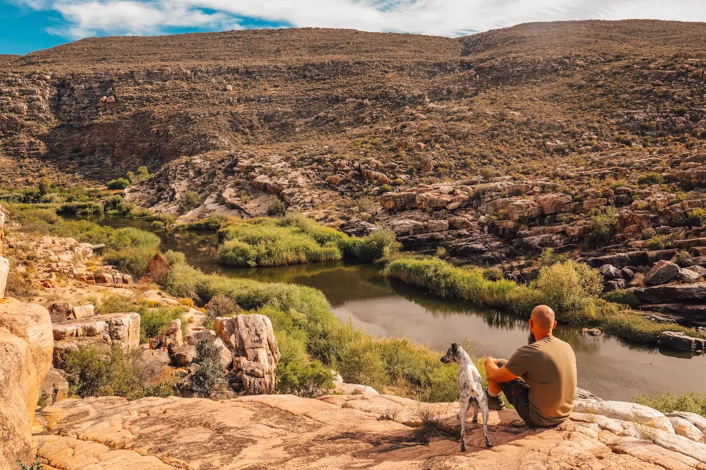 Guest and dog sitting on rocks above the Cederberg river on 1,350 hectares of private land, Bliss & Stars retreat, Western Cape